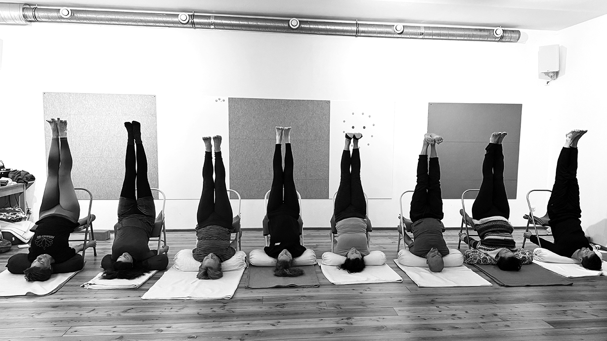 8 Schülernnen und schüler übern Viparita Karani im Stuhl, in einer Reihe