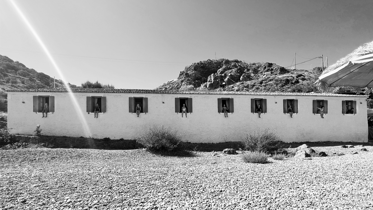 Kleines Hotel am Kiesstrand, gutgelaunte Frauen sitzen in den Fenstern und lassen die Beine rausbaumeln