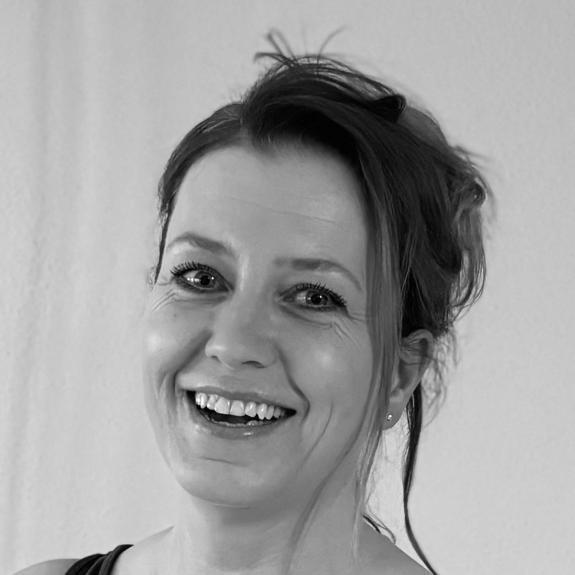 Dunkelhaarige Frau mit hochgesteckten Haaren lacht in die Kamera, Portraitaufnahme