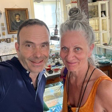 Monika und Theophilos stehen in einem Laden auf Lesbos und blicken in die Kamera