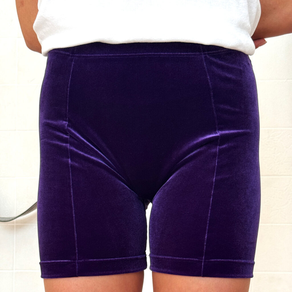 Yoga-Übende mit kurzer lila Samthose und weißem T-Shirt