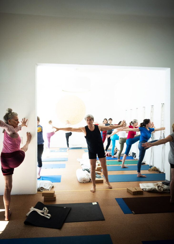 Glenn Ceresoli steht mit ausgebreiteten Armen im Yogashala und leitet eine Gruppe von Schüler*innen an