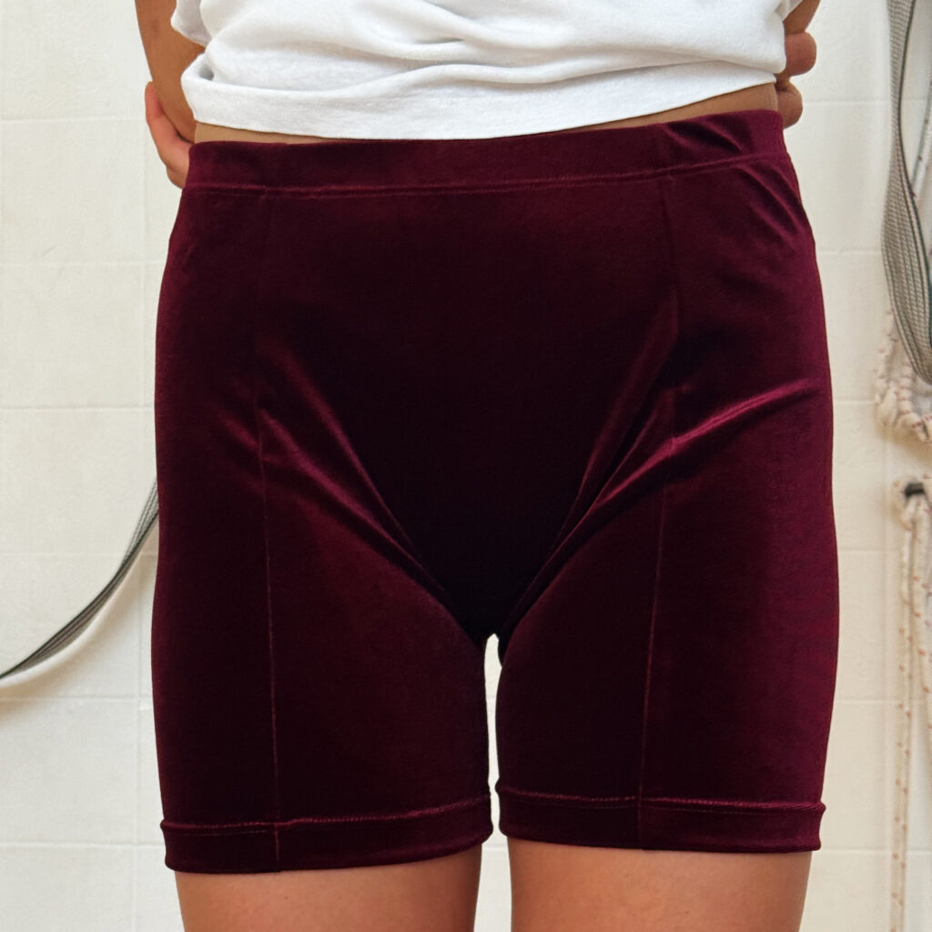 Yoga-Übende mit kurzer weinroter Samthose und weißem T-Shirt