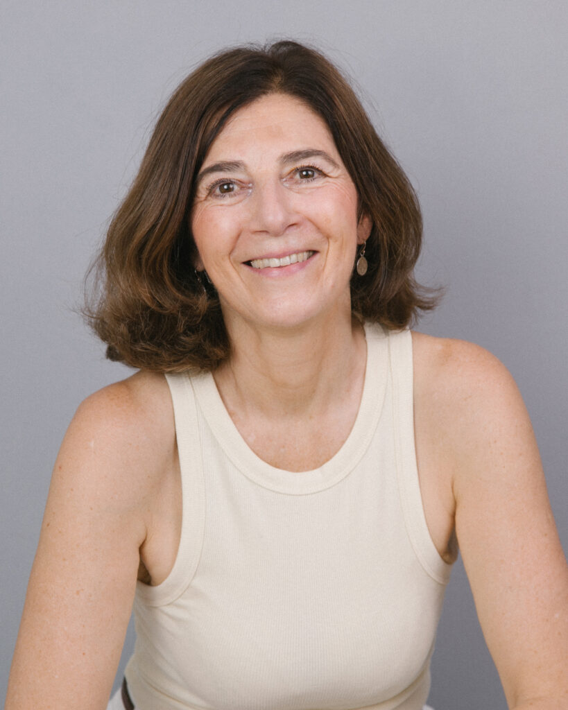 Eine dunkelhaarige sportliche Frau im cremefarbenen ärmellosen Top lächelt in die Kamera